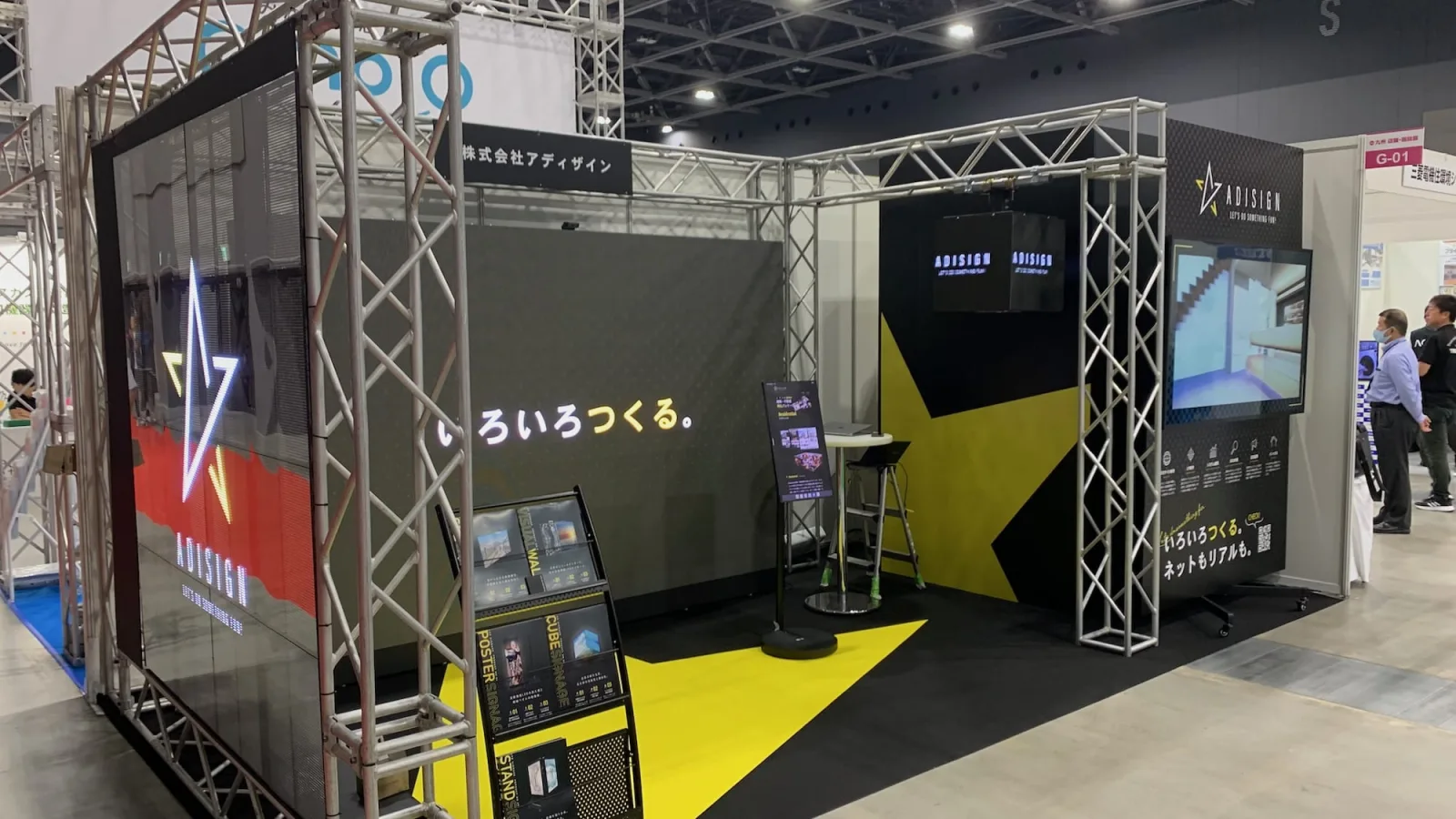 アディザネージの自社出展ブース。通路側にシースルーのLEDビジョン、奥の壁一面にLEDビジュアルウォール、右奥に大型の液晶モニター、上部にキューブ型のLEDサイネージを置いている
