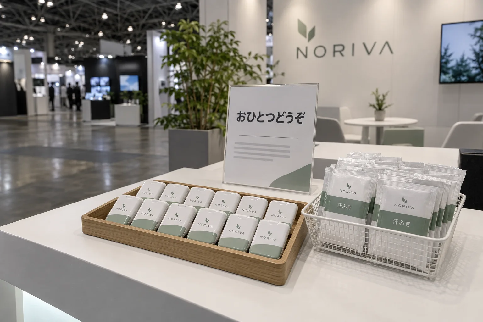 展示会ブースの受付カウンターに、ロゴ入りのミントタブレットのケースと個包装の汗拭きシートを並べ、「おひとつどうぞ」の札を立てている